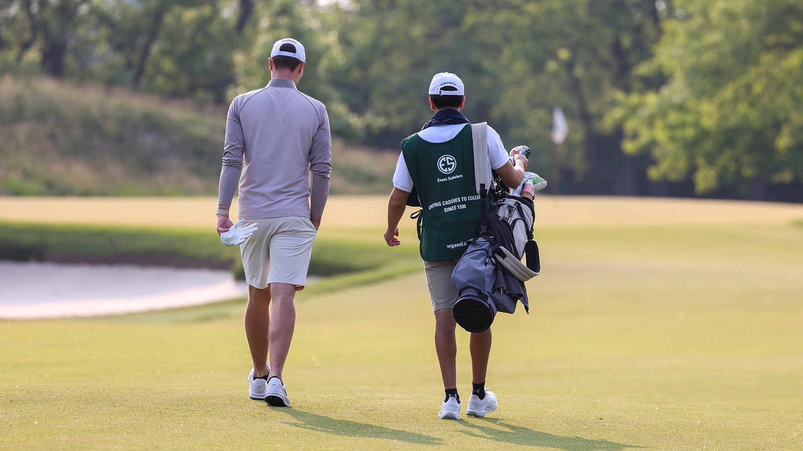 Golfer and caddie walk down a fairway